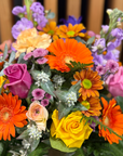 Close up of colorful box of assorted flowers including orange gerberas, pink and yellow roses, and mauve stock.