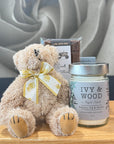 Teddy bear with a bow and a candle labeled 'Ivy & Wood' and Chocolate Bar on a wooden surface.