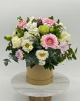 A floral arrangement of mixed flowers in pastel colors, presented in a round hat box.
