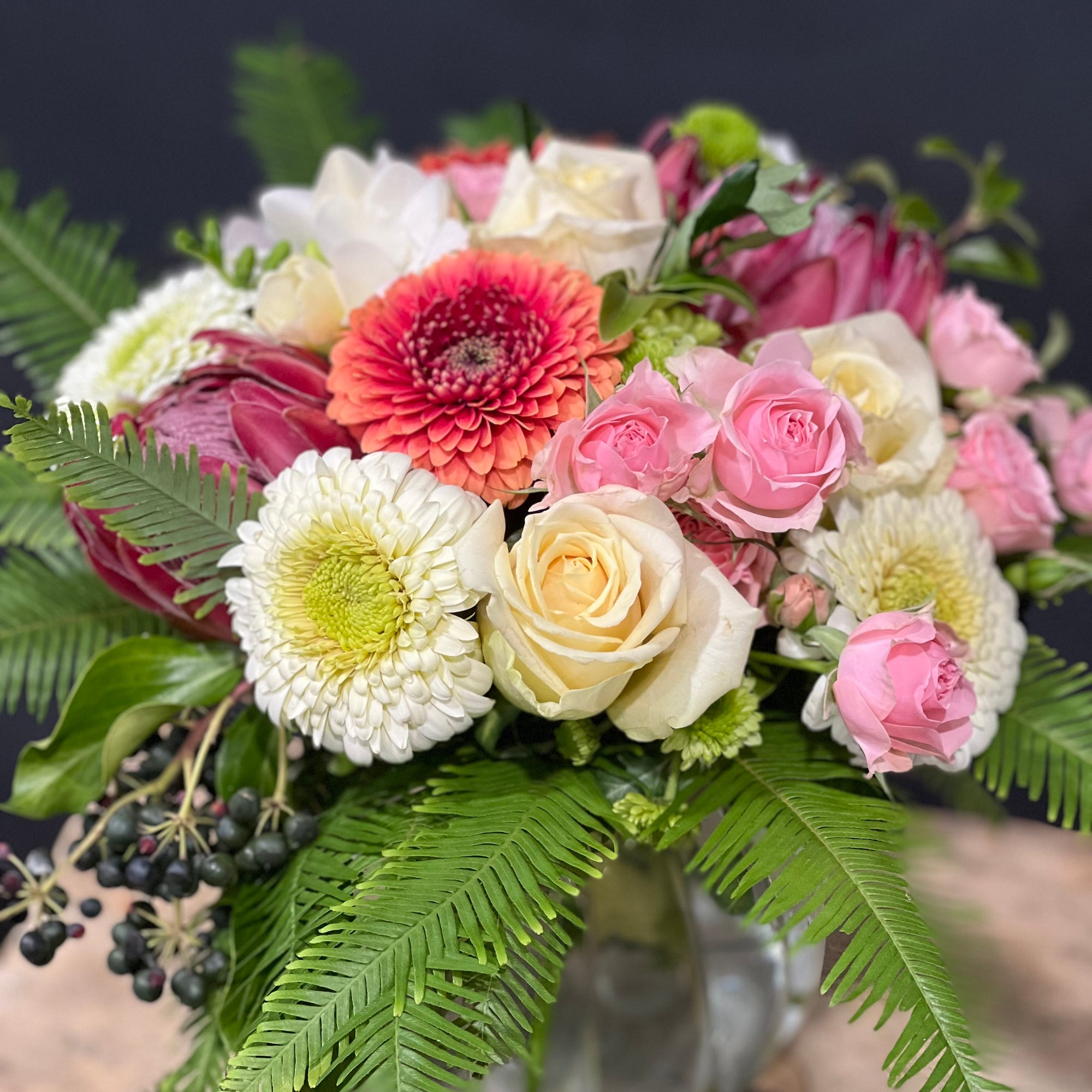 Assorted flowers and foliage in a glass posy vase against a grey background
