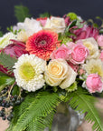Assorted flowers and foliage in a glass posy vase against a grey background