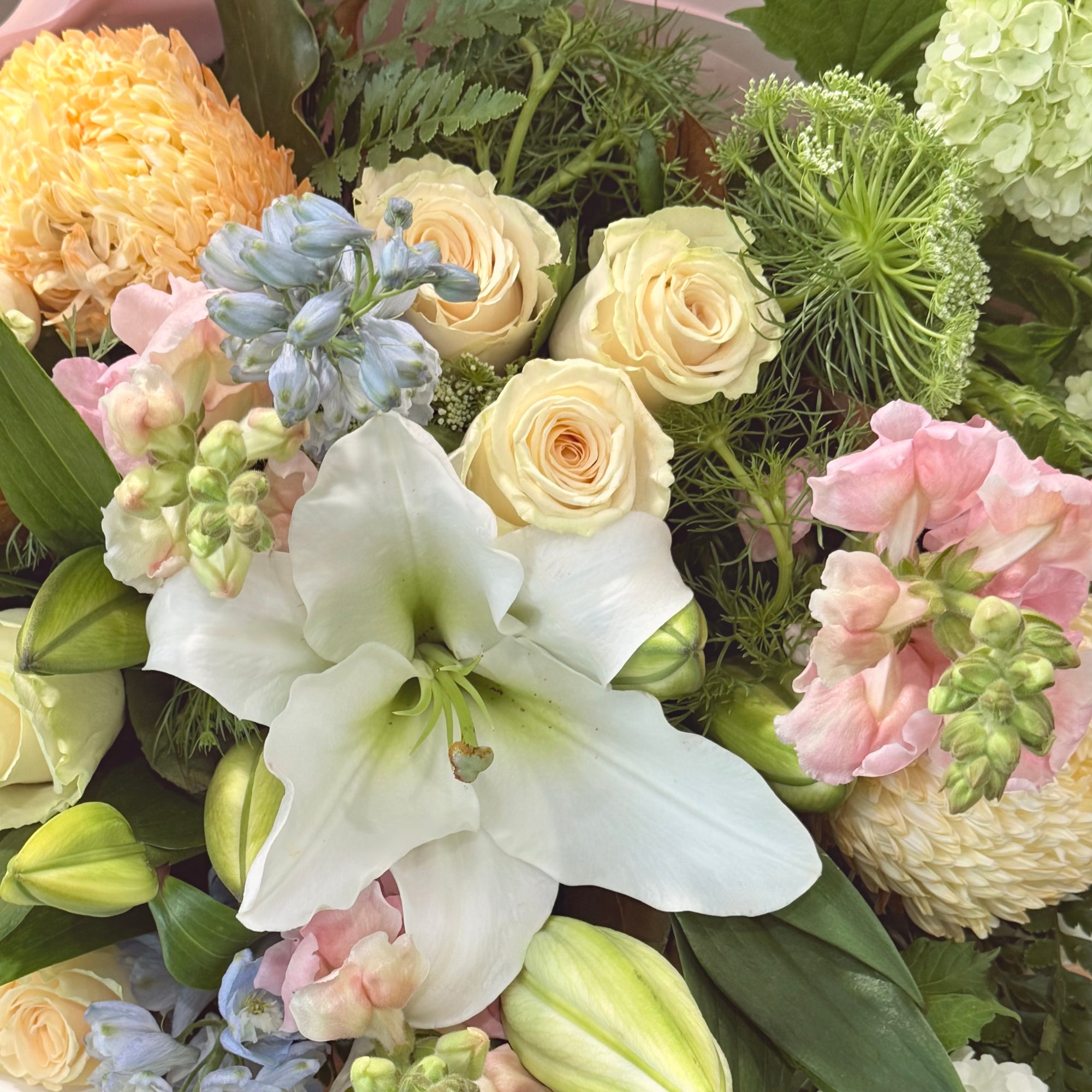 Close up image of Cream roses, blue delphinium, white Lilles, Pale pink snapdragons