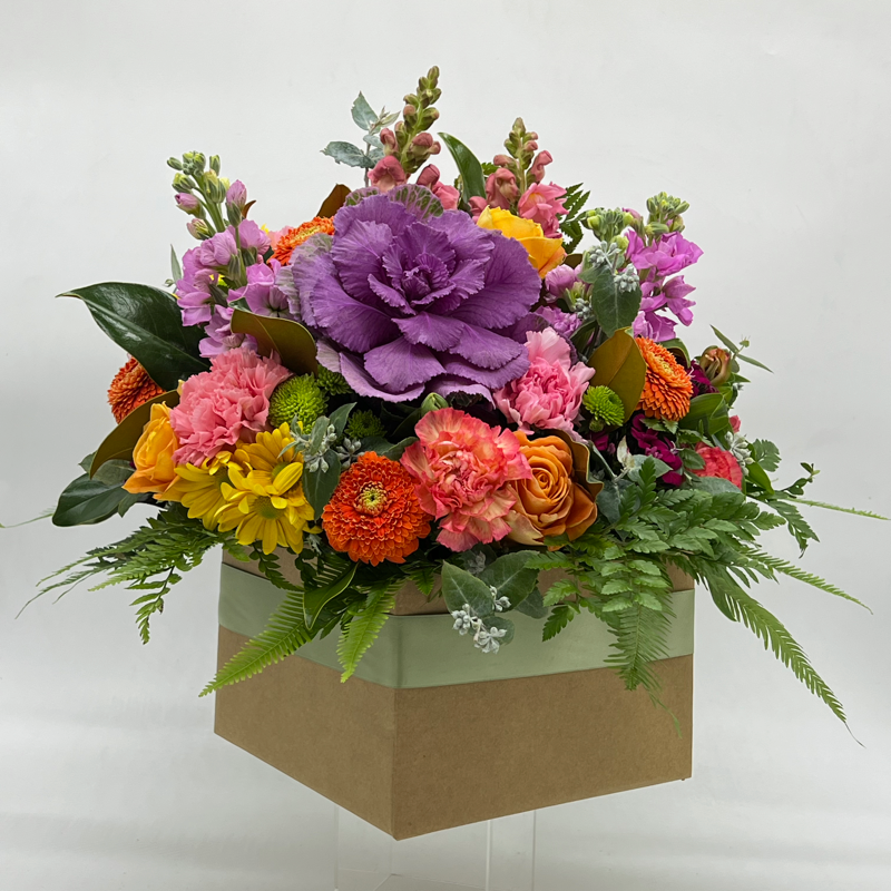 A large box arrangement of assorted seasonal flowers featuring shades of purple, pink, orange, yellow, and green foliage.