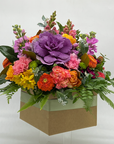 A large box arrangement of assorted seasonal flowers featuring shades of purple, pink, orange, yellow, and green foliage.