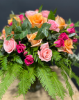 Glass Mason jar of roses, including spray roses with gum foliage and ferns on a grey background.