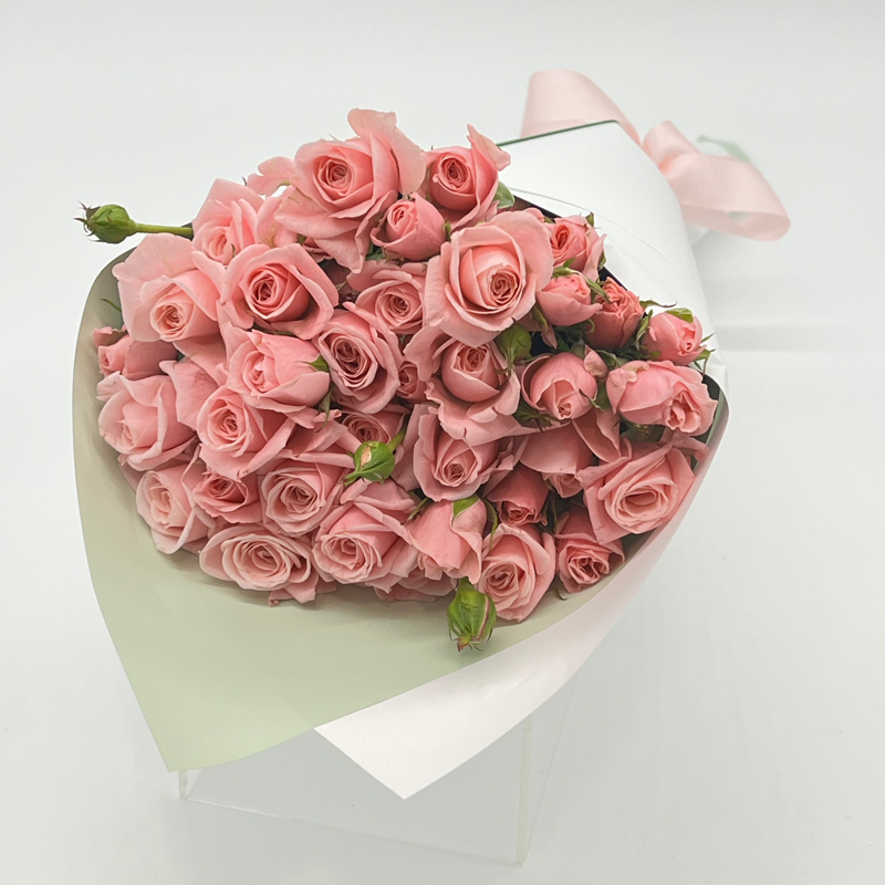 A bouquet of pink spray roses wrapped in white paper with a pink ribbon.