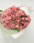 A bouquet of pink spray roses wrapped in white paper with a pink ribbon.