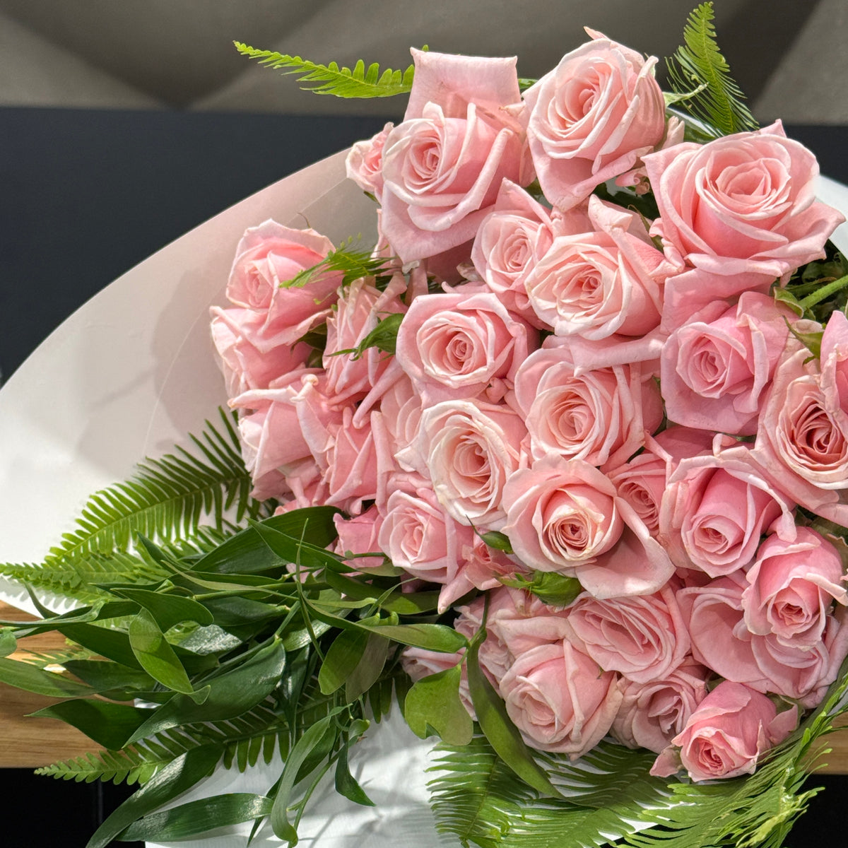 A bouquet of light spray pink roses with green  foliage, wrapped in white paper and photographed close up.