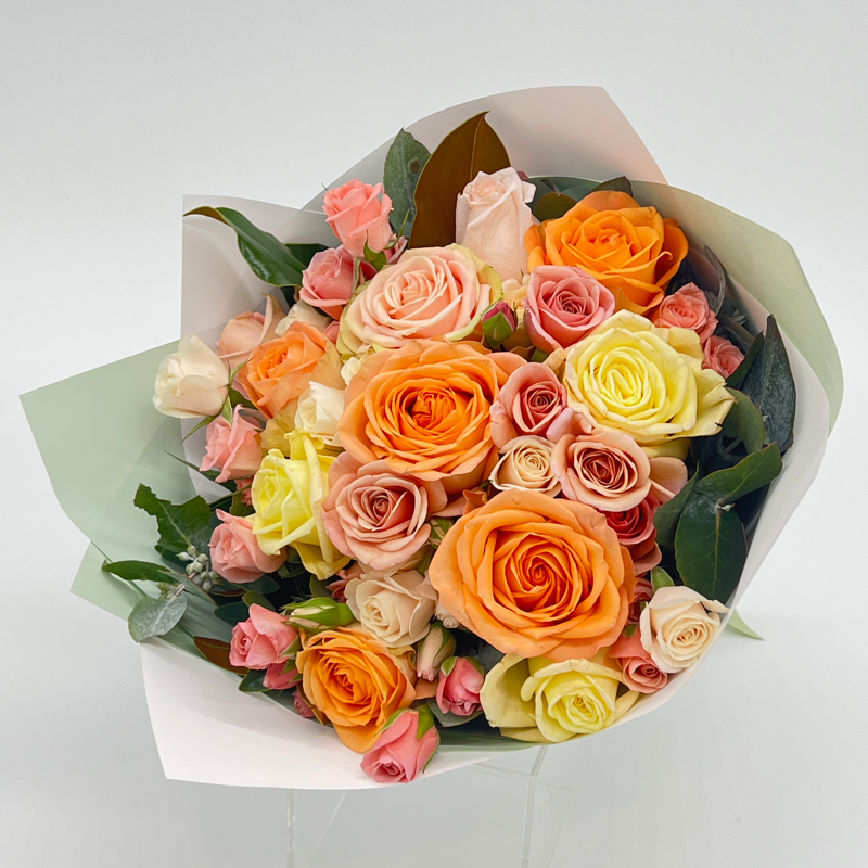 A short posy of twenty multi-coloured roses wrapped in simple paper with seasonal foliage.