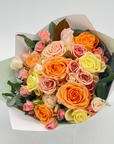 A short posy of twenty multi-coloured roses wrapped in simple paper with seasonal foliage.