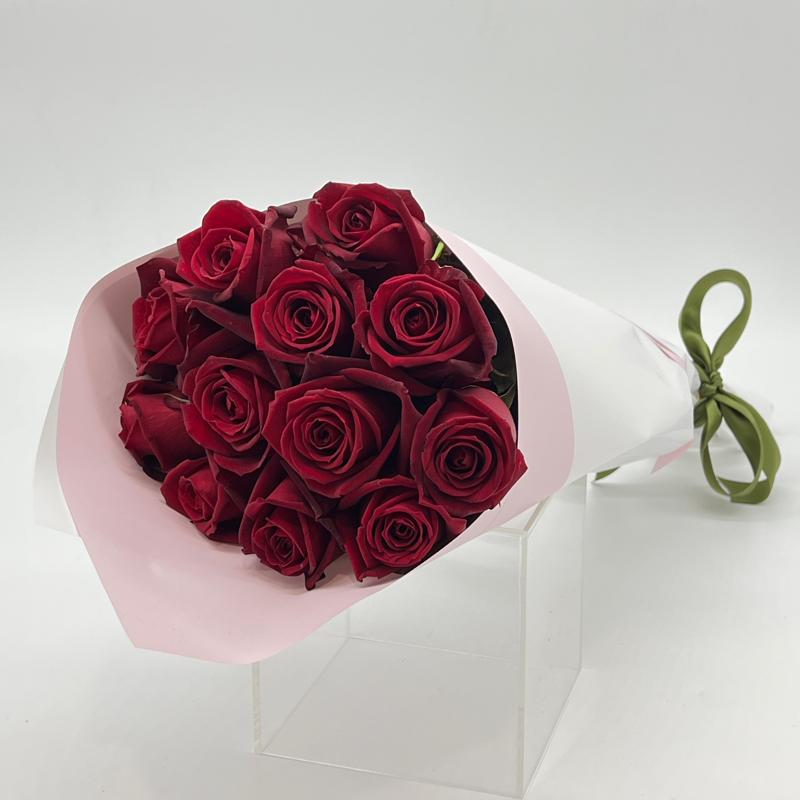 A bouquet of 12 long stemmed red roses, elegantly wrapped in white paper with a green ribbon.