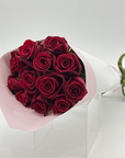 A bouquet of 12 long stemmed red roses, elegantly wrapped in white paper with a green ribbon.