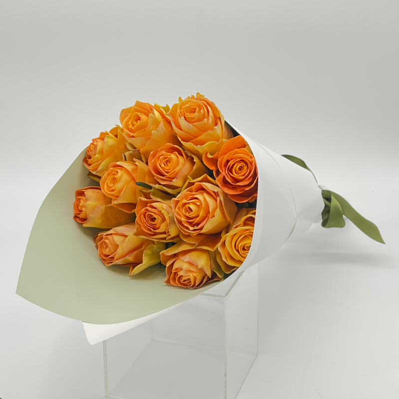 A bouquet of long stemmed orange roses presented in a white wrapping paper.