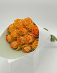 A bouquet of long stemmed orange roses presented in a white wrapping paper.