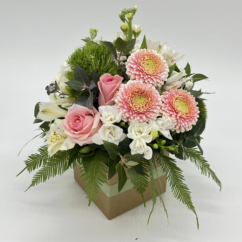 A small square box floral arrangement with an assortment of pink, white, and green flowers.