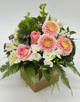 A small square box floral arrangement with an assortment of pink, white, and green flowers.