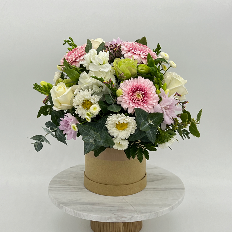 A floral arrangement of mixed flowers in pastel colors, presented in a round hat box.