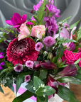 Small box of pink and purple flowers with green leaves on a blurred background